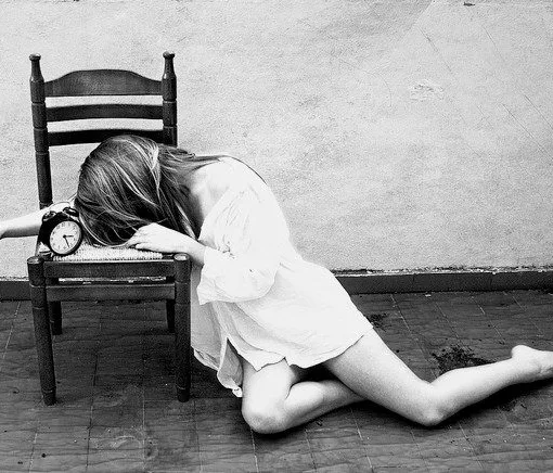 Mujer joven recostada junto a un despertador antiguo en una habitación de madera